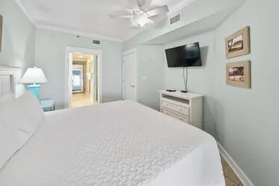 a white bedroom with a bed and a flat screen tv at Grand Panama 207 in Panama City Beach