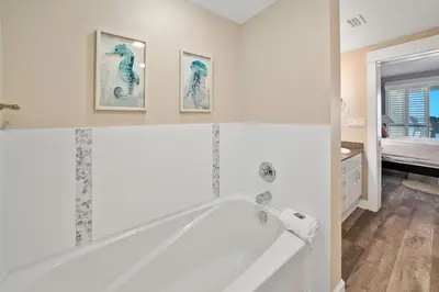 a white bathroom with a tub and three pictures on the wall at Grand Panama 501 in Panama City Beach