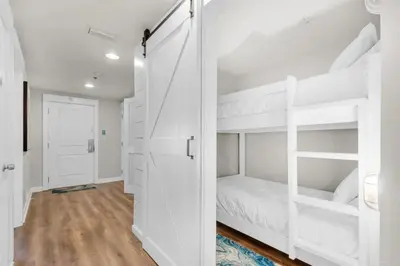 a bedroom with white bunk beds and a hallway at Grand Panama 604 in Panama City Beach
