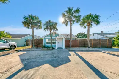 a house with palm trees in front of a fence at Tiki Palms Paradise by Emerald Coast Retreats in Panama City Beach