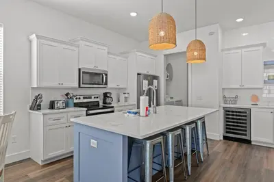 a kitchen with white cabinets and a island with bar stools at Laid-Back - Private Pool, 4 Min Walk to Beach, Close to 30A, FREE Daily Activities in Panama City