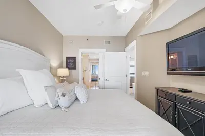 a bedroom with a large white bed with a flat screen tv at Grand Panama 1003 in Panama City Beach