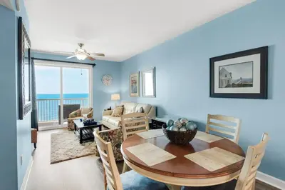 a dining room with a table and a living room with the ocean at Grand Panama 1806 in Panama City Beach
