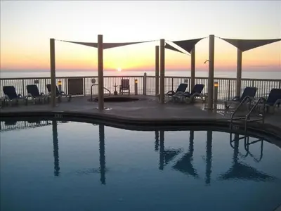 a swimming pool with chairs and a sunset in the background at Sunrise 2401 in Panama City Beach