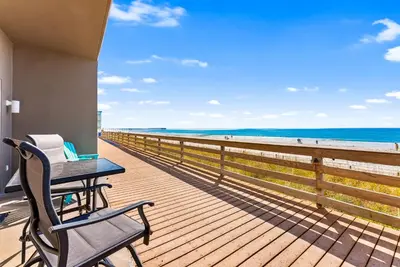 a table and a chair on a deck with the beach at Tidewater Resort! Ground Floor! Free Beach Chairs! by Dolce Vita Getaways PCB in Panama City Beach