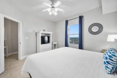 a white bedroom with a bed and a television at Celadon Beach 2107 in Panama City Beach