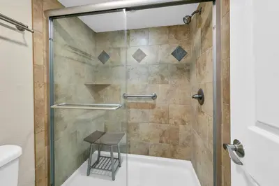 a shower with a glass door and a stool in a bathroom at Dunes of Panama 1104E in Panama City Beach