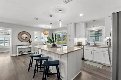 a kitchen with white cabinets and blue bar stools at Blue Tide Hideaway - Golf Cart, Sznl Hot Tub, Pets OK, FREE Daily Activities, & More! in Panama City