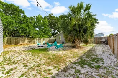 a backyard with a palm tree and chairs and a fence at Sunset Haus in Panama City Beach