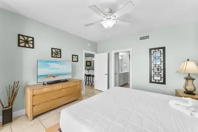 a white bedroom with a bed and a flat screen tv at Treasure Island #1102 in Panama City Beach