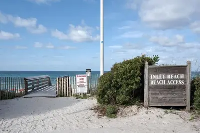 a sign on a beach with the ocean in the background at A Wave From It All Bikes Lake Grill in Inlet Beach