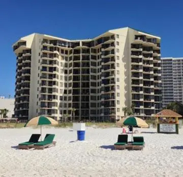 a building on the beach with chairs and umbrellas at Pelican's Perch at the Sunbird in Panama City Beach