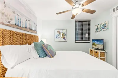 a bedroom with a white bed and a ceiling fan at Pelican's Perch at the Sunbird in Panama City Beach