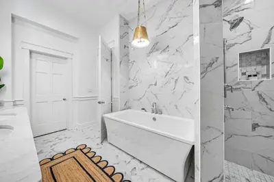 a white bathroom with a tub and marble walls at Shell Of A View Cottage And Carriage House in Rosemary Beach