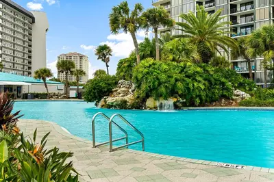 a swimming pool with a waterfall and palm trees at 2BD Edgewater Beach & Golf Resort! Best Amenities! by Dolce Vita Getaways PCB in Panama City Beach