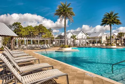 a swimming pool with lounge chairs and palm trees at Whale Tales Prominence 30A! BESIDE POOL! 6 seater LSV! 4 Bikes Sleeps 6! in Watersound Beach