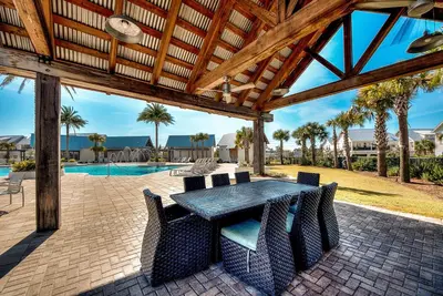 a patio with a table and chairs and a pool at Whale Tales Prominence 30A! BESIDE POOL! 6 seater LSV! 4 Bikes Sleeps 6! in Watersound Beach