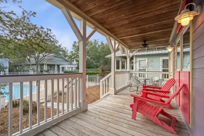 a porch with two red chairs and a table at Peacock Cottage in Inlet Beach