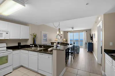 a kitchen with white cabinets and a dining room with the ocean at Calypso 2-2108 West in Panama City Beach