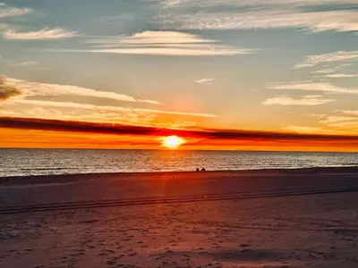 a sunset on the beach with a person in the water at A Wave From It All in Laguna Beach Large Patio Sleeps 4 Dog Ok in Panama City Beach