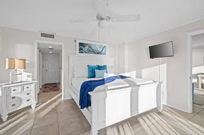 a white bedroom with a bed and a tv at Commodore 410 in Panama City Beach