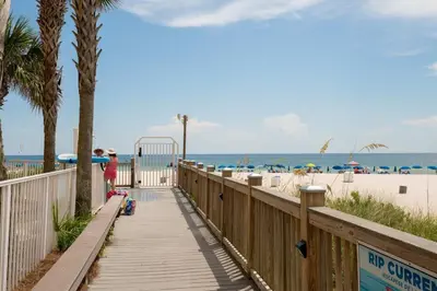 a woman walking down a wooden walkway to the beach at Sterling Reef 503 - Pierview Oasis - Sleeps 6 in Panama City Beach
