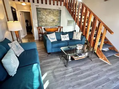 a living room with a blue couch and a staircase at Horizon South 33D - Sunstead Retreat - Sleeps 6 in Panama City Beach