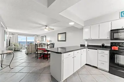 a kitchen with white cabinets and a living room with a table at Regency Towers 207 - Sleeps 8 -East-Gulf Overview in Panama City Beach