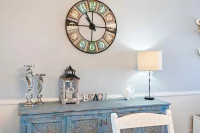 a clock on a wall above a table with a chair at Moondrifter 205 - Sand-Side Oasis - Sleeps 6 in Panama City Beach