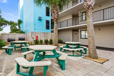 a patio with picnic tables and palm trees in front of a building at Sand-Crest Overlook - Moondrifter 201 in Panama City Beach