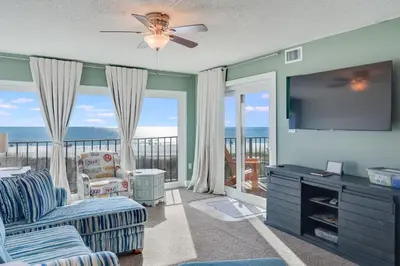 a living room with a flat screen tv and a balcony at Sand-Crest Overlook - Moondrifter 201 in Panama City Beach