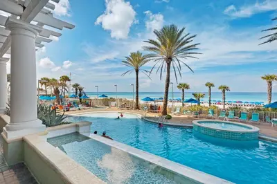 a pool at a resort with palm trees and the ocean at Boardwalk 2101 in Panama City Beach