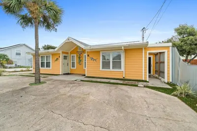 a yellow house with a palm tree in front of it at Spacious Dog-Friendly Unit with Game Room & Private Yard, Walk to East PCB Beach in Panama City Beach