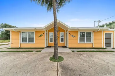 a yellow house with a palm tree in the driveway at Spacious Dog-Friendly Duplex w/ Bonus Game Room & Private Backyard Near Beach in Panama City Beach
