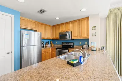 a kitchen with wooden cabinets and a stainless steel refrigerator at Gulf-Front Corner Unit! Stunning Coastline Views! by Dolce Vita Getaways PCB in Panama City Beach