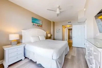 a white bedroom with a white bed and a bathroom at 21st-Floor Sunrise Beach Gulf-Front Condo w/ Bunks & Panoramic Views in Panama City Beach