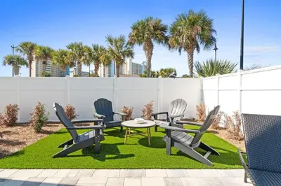 a patio with three chairs and a table on grass at New 6BR Home Sleeps 20 | Private Pool, Walk to Beach, Near Pier Park in Panama City Beach