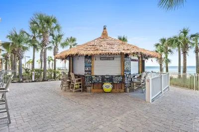 a hut with chairs and a table and palm trees at Calypso Resort by Panhandle Getaways in Panama City Beach