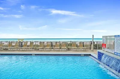 a swimming pool with chairs and the ocean in the background at Emerald Isle by Panhandle Getaways in Panama City Beach