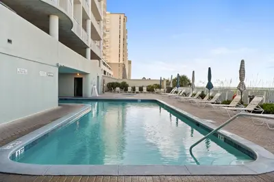 a swimming pool with chairs and a building at Ocean Ritz by Panhandle Getaways in Panama City Beach