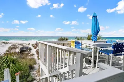 a deck with a table and an umbrella and the beach at Sailfish by Panhandle Getaways in Panama City Beach
