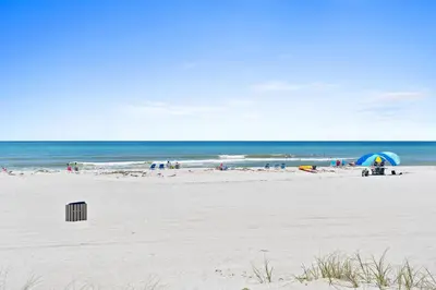 a group of people on a beach with a blue umbrella at Sailfish by Panhandle Getaways in Panama City Beach