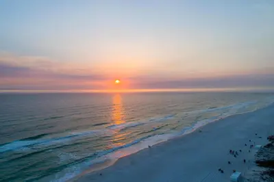 a sunset over the ocean with people on the beach at Shores of Panama by Panhandle Getaways in Panama City Beach