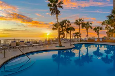 a swimming pool with palm trees and a sunset at Splash Beach Resort by Panhandle Getaways in Panama City Beach