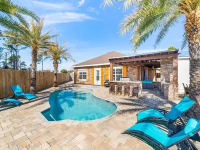 a patio with a swimming pool with blue chairs and a house at Orange Crush in Panama City Beach