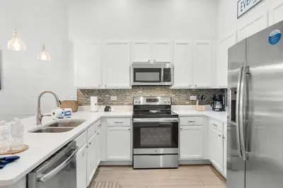 a kitchen with white cabinets and a stainless steel refrigerator at The Village Happy Life Condo - Private Beach Access Pool & Hot Tub in Rosemary Beach