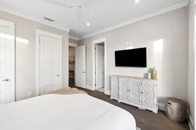 a white bedroom with a bed and a flat screen tv at Four Blue Palms by 30A Escapes in Seacrest