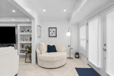 a white living room with a chair and a tv at Gulf Highlands #177 by Nautical Properties in Panama City Beach