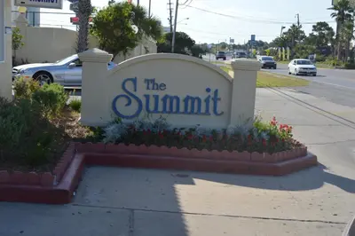 a sign for the summit on a street with flowers at The Summit Condominiums in Panama City Beach