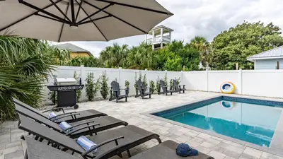 a patio with chairs and an umbrella next to a pool at Modern 5BDR w Private Pool 2 min Walk to the Beach Montoute by AvantStay in Panama City Beach